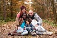 Image of a mother, father, and three children sitting together on a leaf-strewn path in the woods.