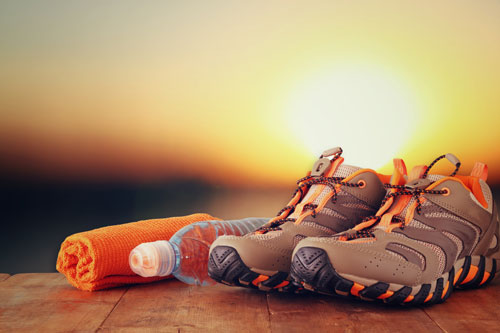 Image of a pair of sneakers, a water bottle, and an orange rolled up yoga mat. There is a sunset in the background.