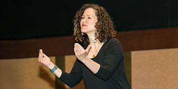 Image of brunette caucasian woman in a black shirt using American Sign Language to communicate.