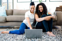 two women sit on the floor using their laptop