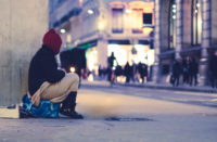 a person experiencing homelessness sits on a sidewalk