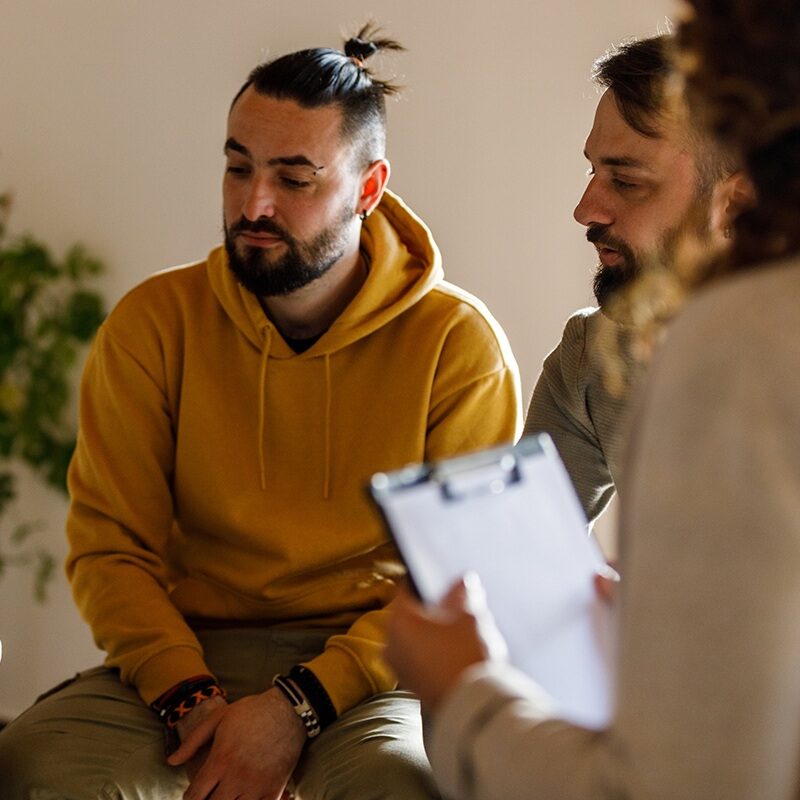 Cut out shot of anxious woman sitting in circle and talking about her mental health struggles with her peers during a group therapy session.