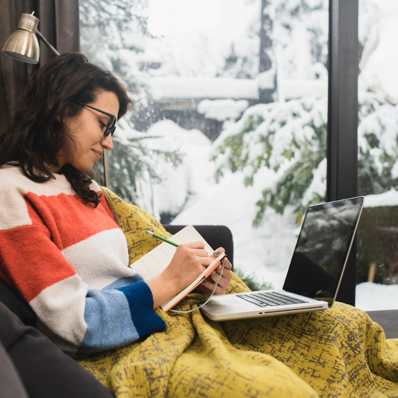2512_STOCK_Woman writing on couch in winter laptop notebook young woman