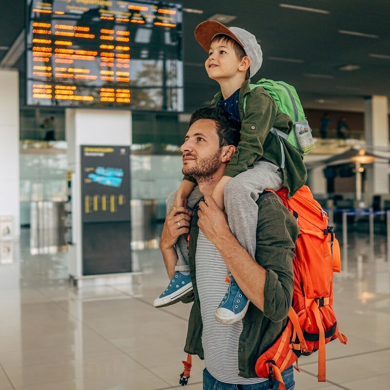 Photo of a cheerful little boy and his father, who travel together waiting for their flight at the airport