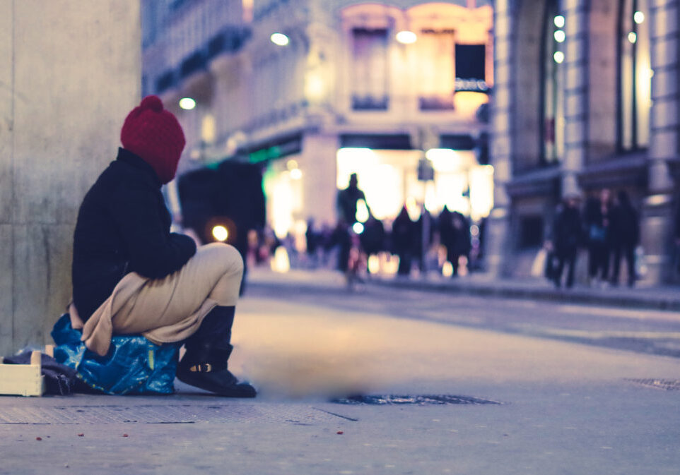 a person experiencing homelessness sits on a sidewalk