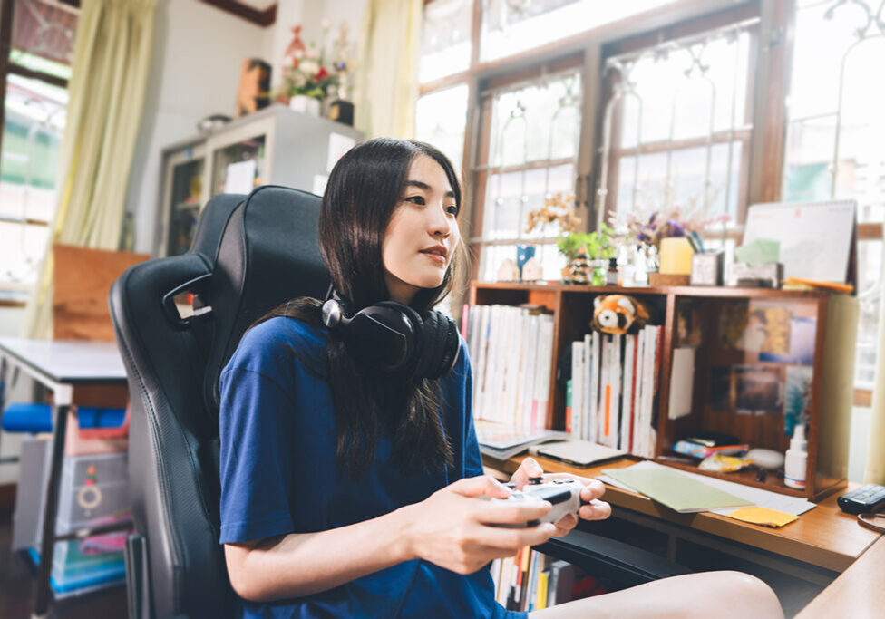 Beautiful young adult asian woman hand holding a joy controller wear headset and play game. People relax and entertainment hobby lifestyle at home concept. Background in domestic room on day.