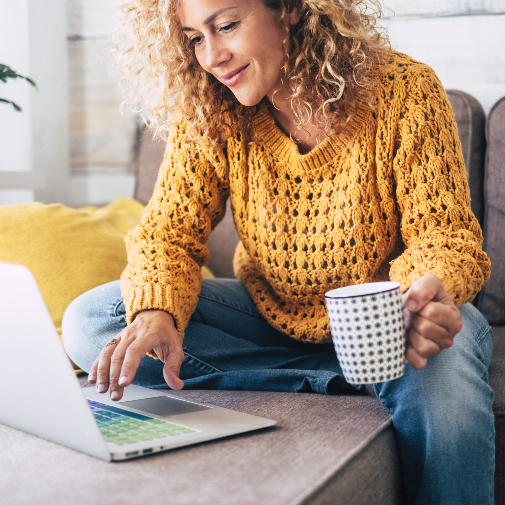 Nice beautiful lady with blonde curly hair work at the notebook sit down on the sofa at home - check on line shops for cyber monday sales - technology woman concept for alternative office freelance