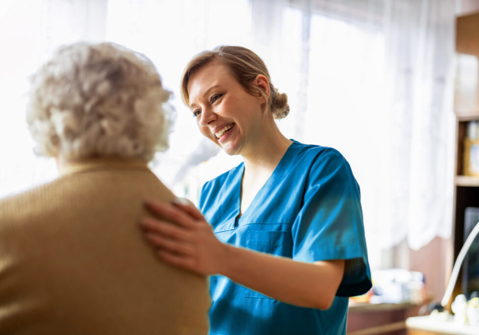 A smiling nurse assists a patient in their room.
